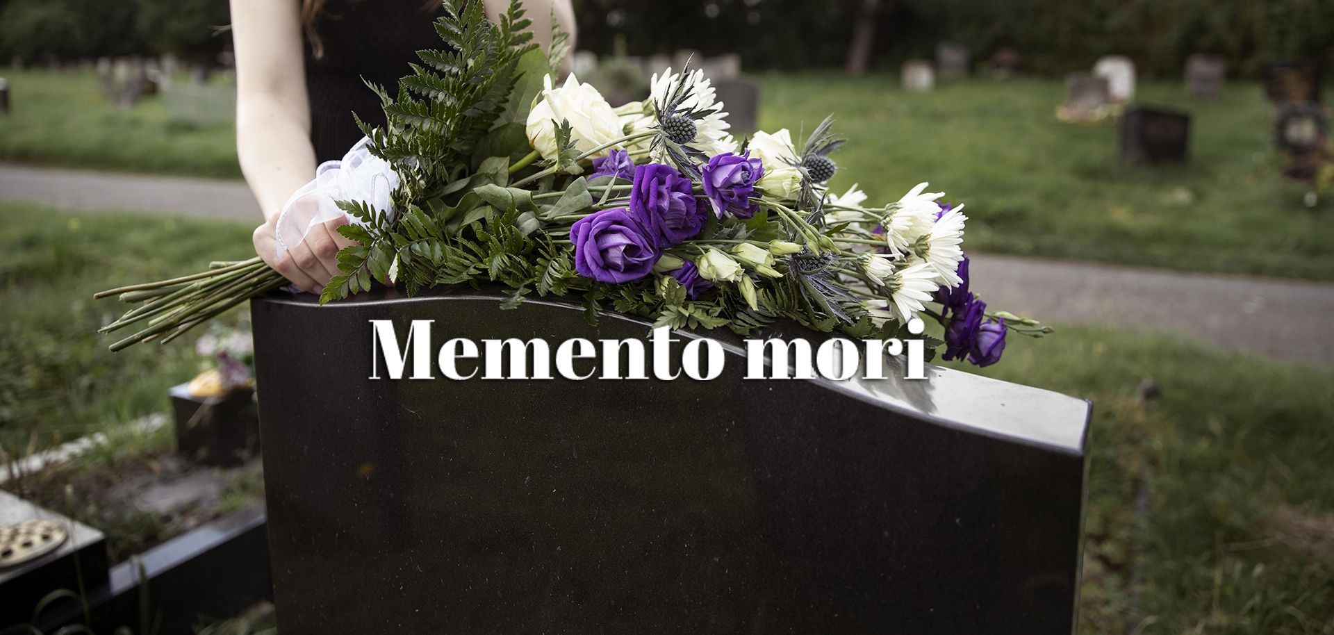 En person lägger en bukett med vita och lila blommor på en gravsten på en grön kyrkogård, med texten ’Memento mori’.